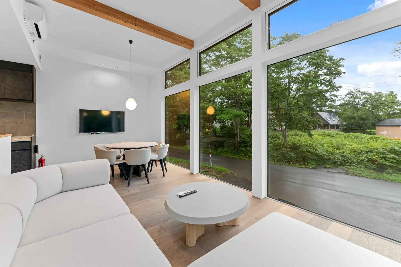 Open living room with large windows onto green summer forest in Niseko